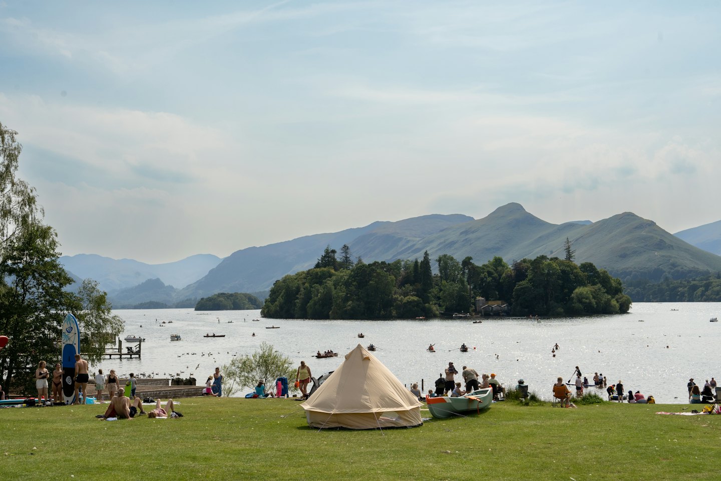 Menschen genießen einen sonnigen Tag am See mit Booten und Bergen.